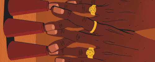 Ilustracja przedstawia zbliżenie dwóch dłoni ułożonych na stole. Palce spoczywają na trzech odwróconych, czerwonych stożkach ustawionych w rzędzie. Na palcach widoczne są złote pierścionki o prostych, okrągłych kształtach. Skóra dłoni ma ciemny odcień, a paznokcie są krótko obcięte. Tło i powierzchnia stołu utrzymane są w ciepłych, brązowych tonach